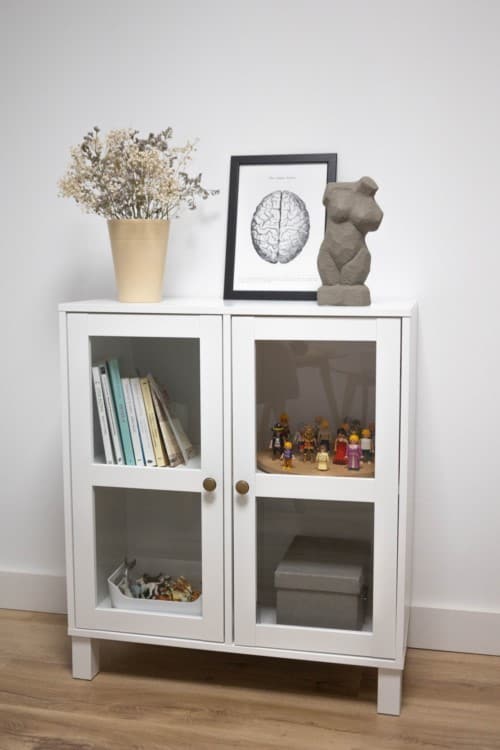 Un mueble blanco con puertas de cristal y un osito de peluche.